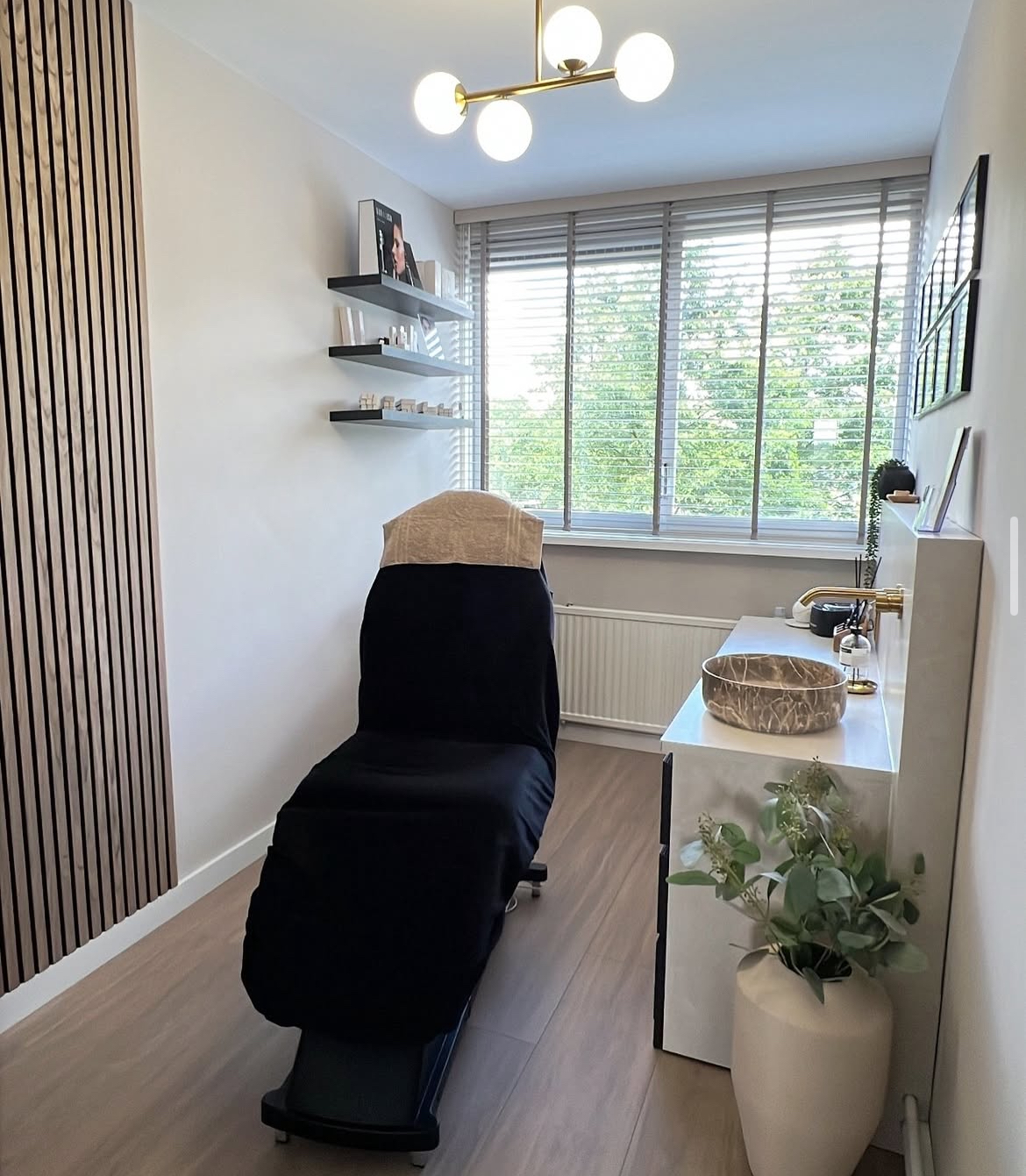 De behandelkamer van The Beauty Addict: behandelbed, houten lattenwand en messing lamp